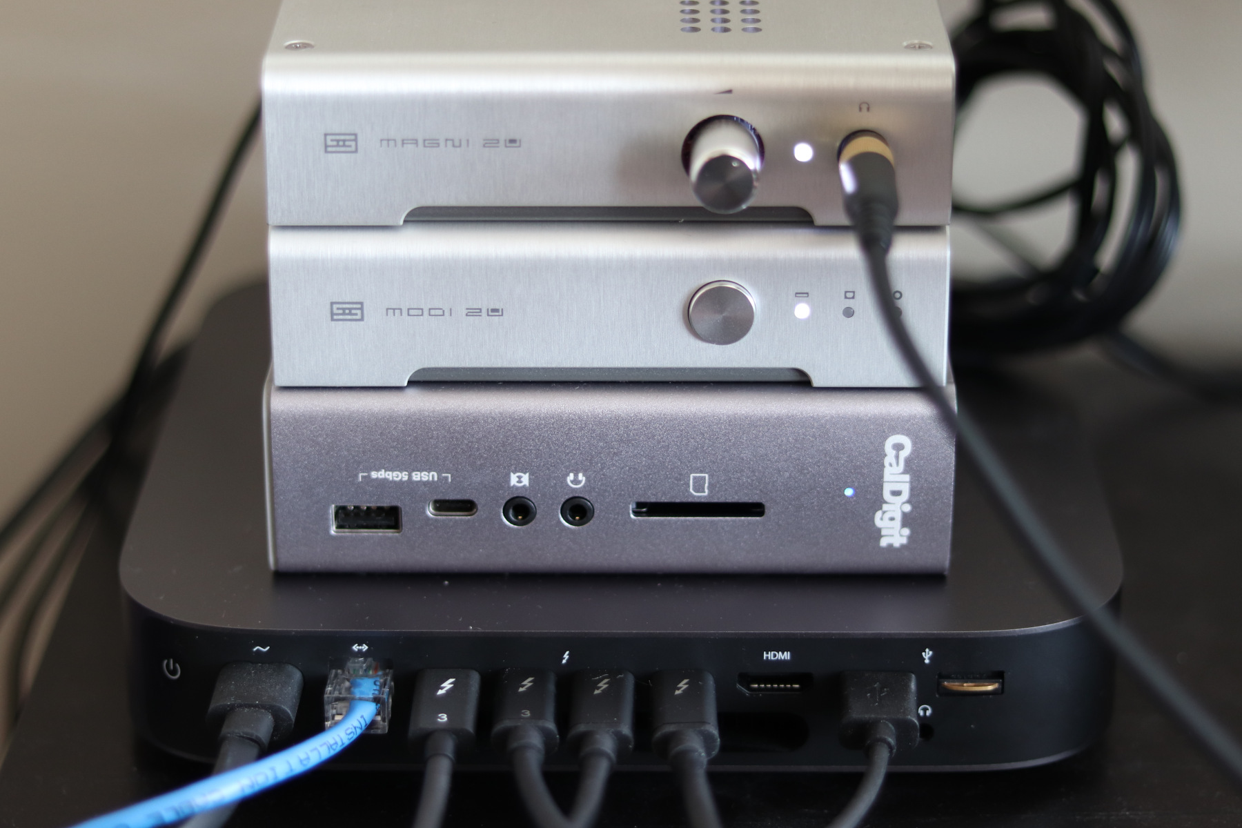 A Mac mini (2018) with several Thunderbolt 3 cables, a Thunderbolt dock above it, and a Schiit Modi 2 Uber and Magni 2 Uber above that